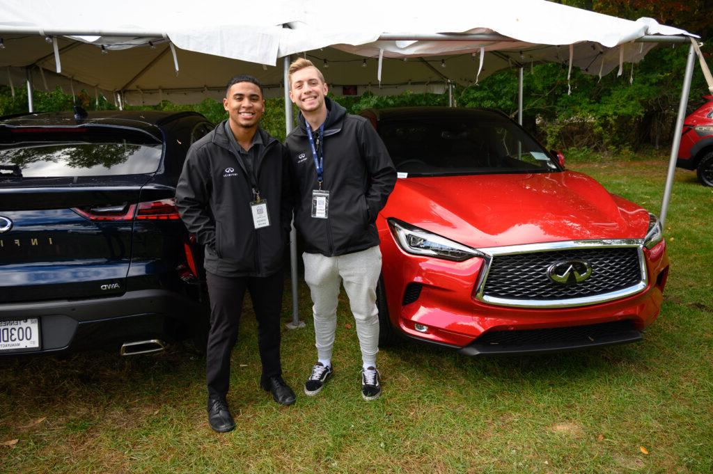 Two students pictured at Auto Show with a red car behind them